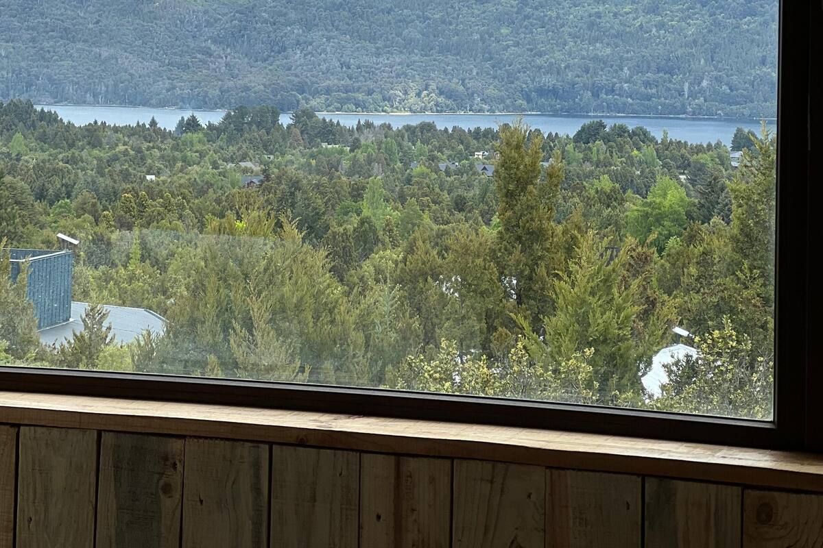 A view from a window overlooking a mountainous landscape with a lake and dense forest.