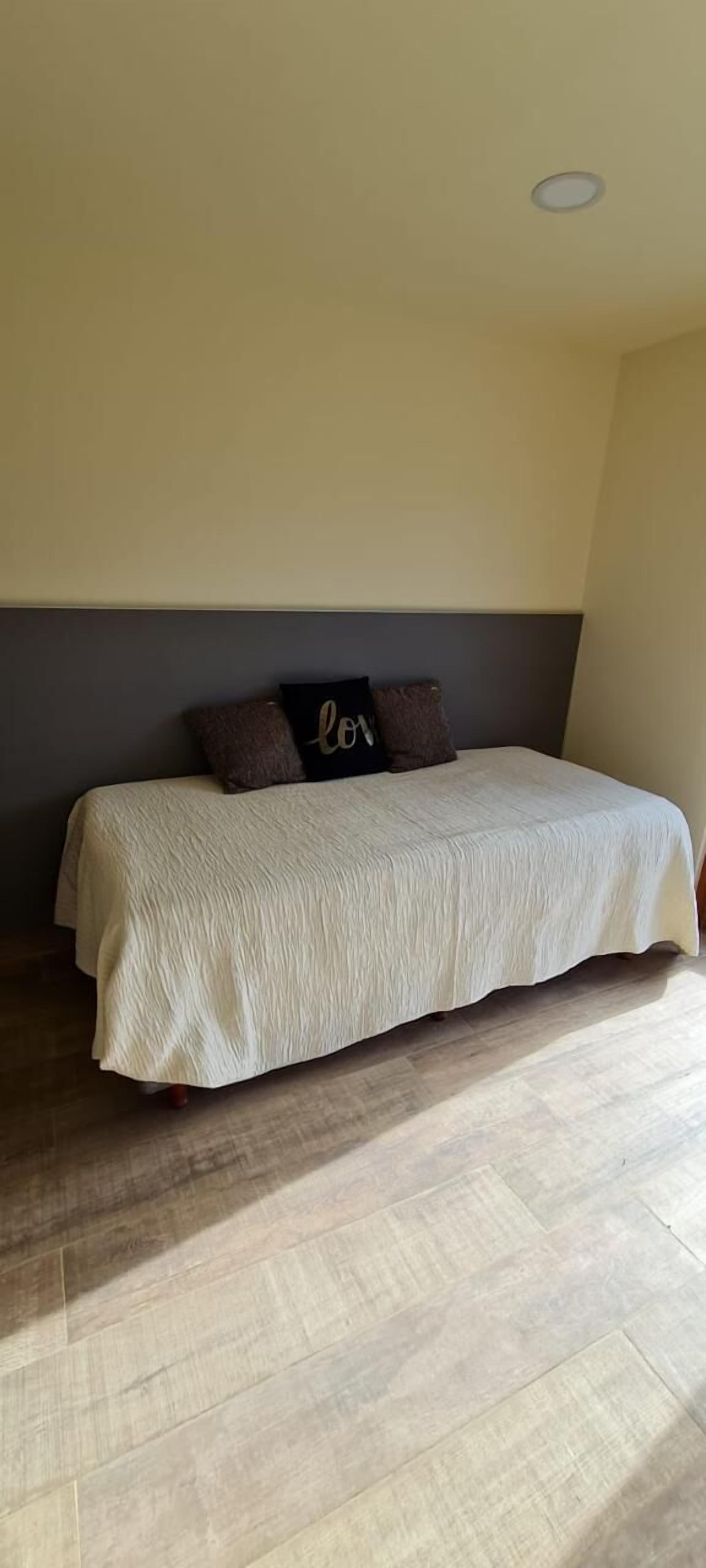 A bedroom with a bed, a headboard, a wall with a recessed ceiling light, and a wooden floor.