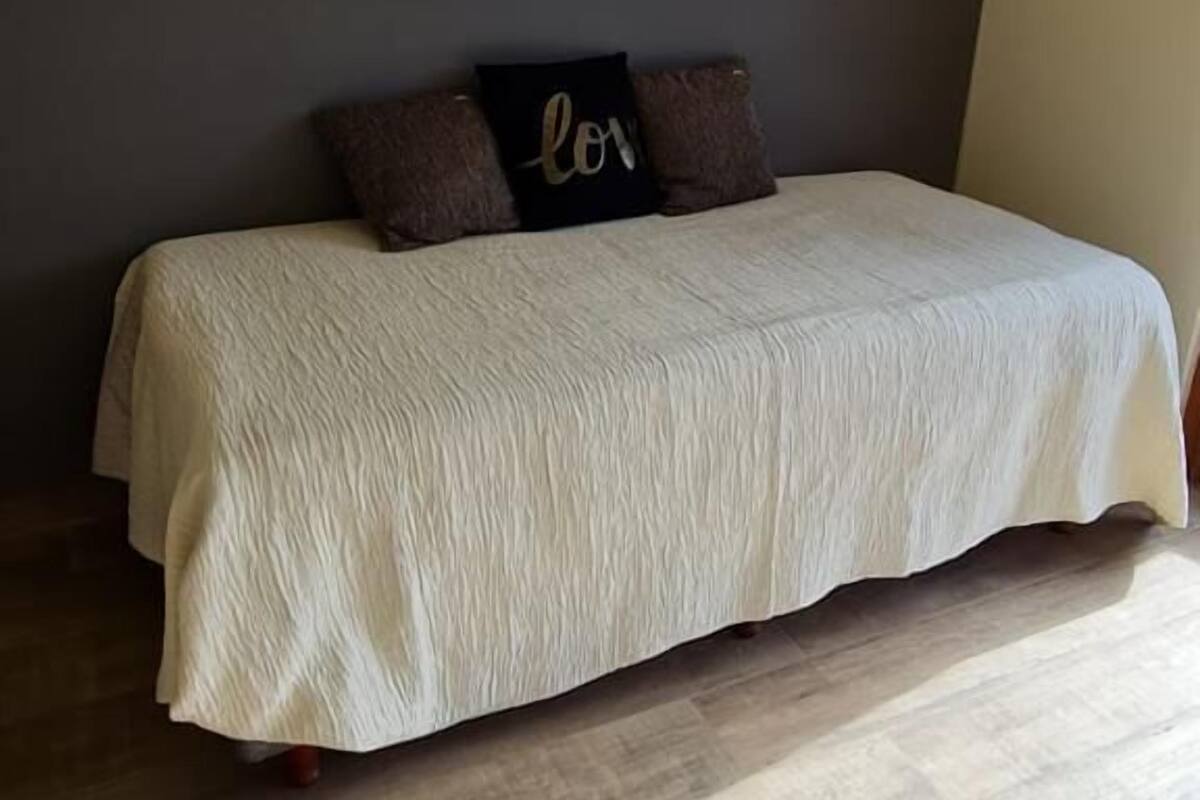 A bedroom with a bed, a headboard, a wall with a recessed ceiling light, and a wooden floor.