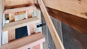 Una escalera de madera con barandilla de metal, vigas de madera y vista del techo.