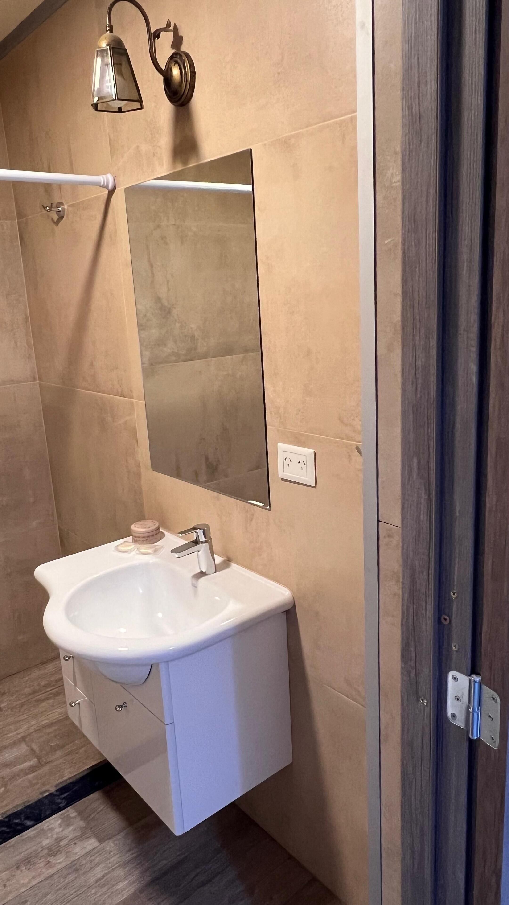 A bathroom with a white sink, a mirror, and a wall-mounted light fixture.