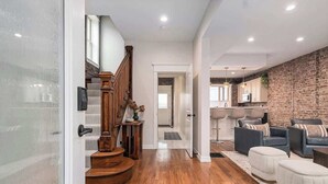 A modern living room with a staircase, wooden flooring, and a brick accent wall.