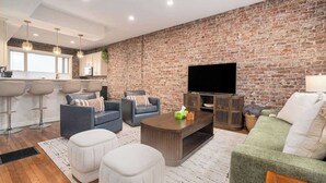A modern living room with a brick wall, a flat-screen TV, and comfortable seating.