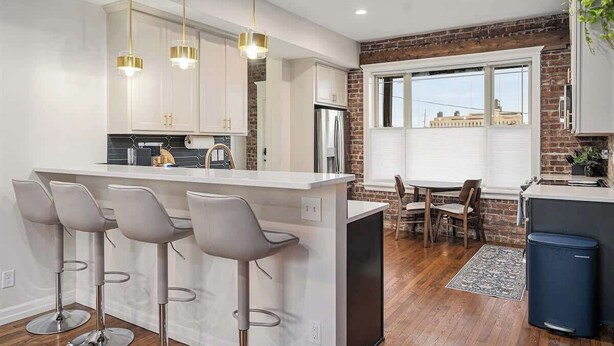 A modern kitchen with a central island, bar stools, and pendant lighting.