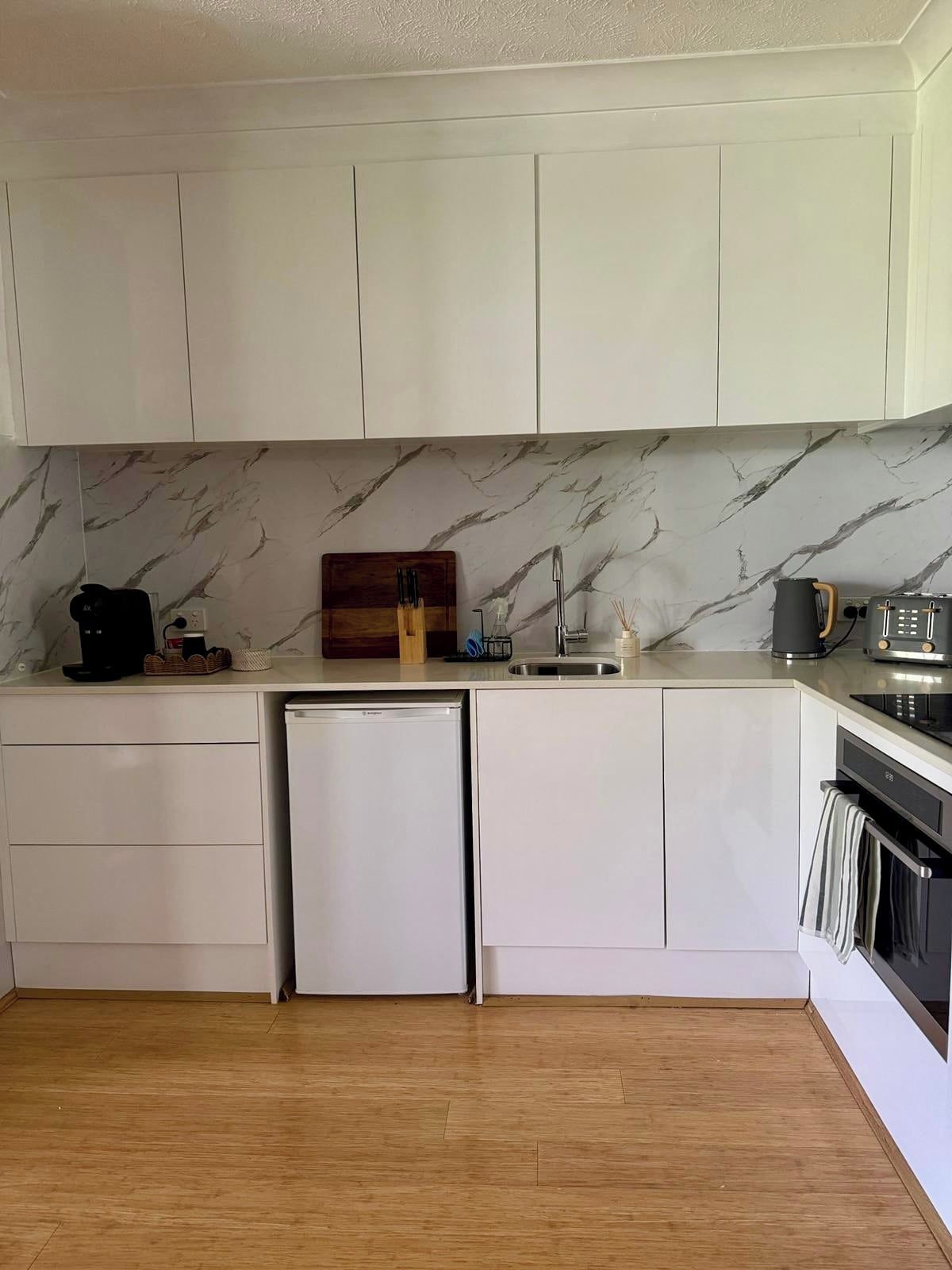A kitchen with white cabinets, a marble backsplash, a built-in dishwasher, and a stove.