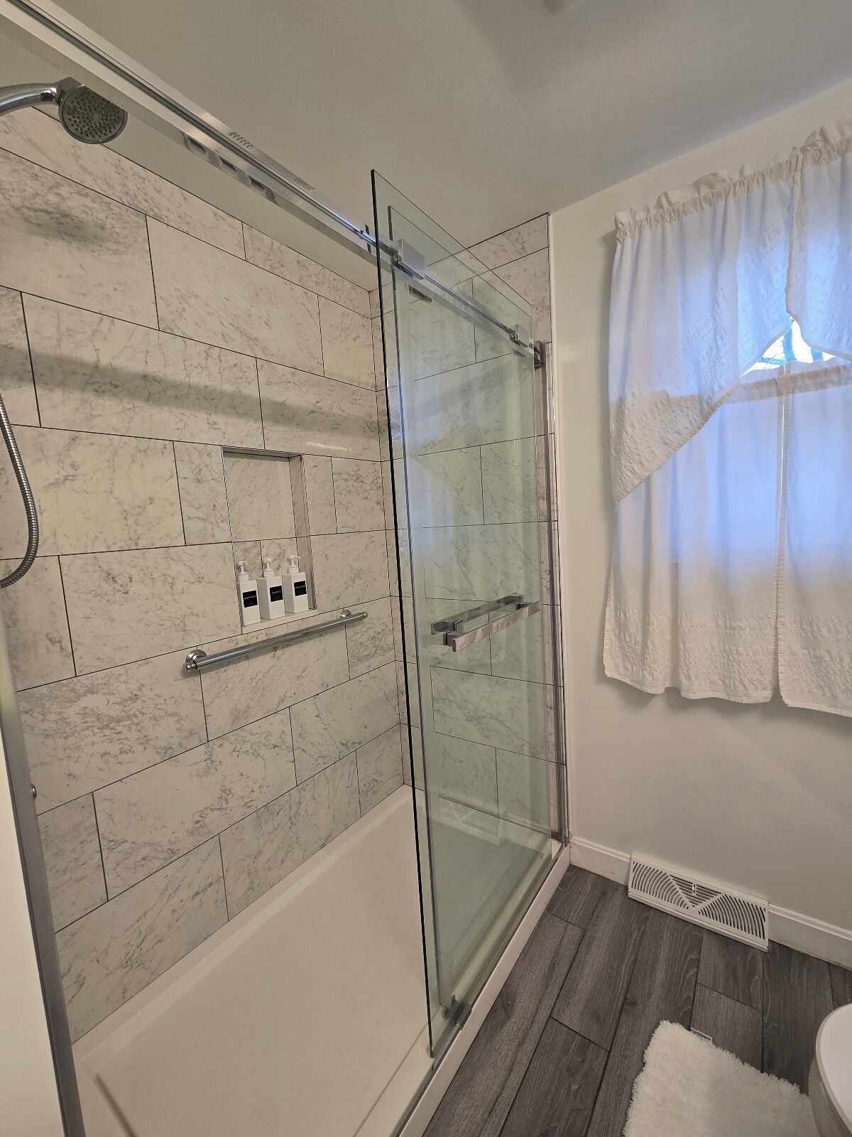 Un baño moderno con cabina de ducha de vidrio, baldosas de mármol y un perchero blanco.
