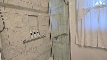 Un baño moderno con cabina de ducha de vidrio, baldosas de mármol y un perchero blanco.