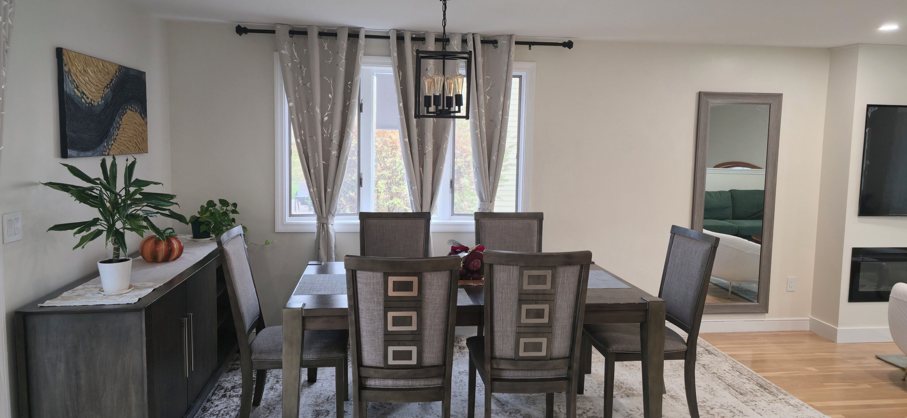 Un comedor con una mesa y sillas, una planta en maceta, un cuadro y un televisor en la pared.