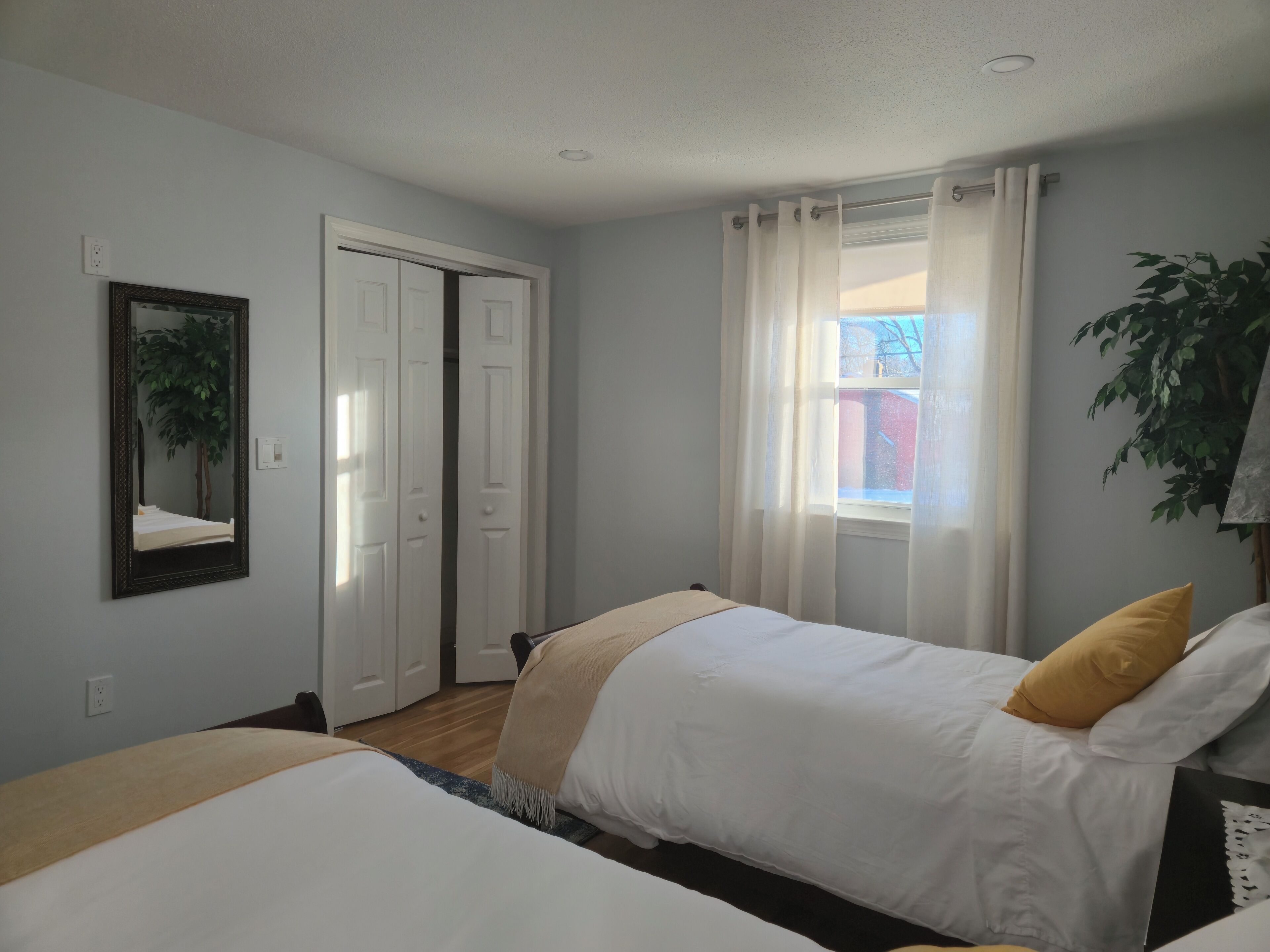 Een slaapkamer met twee bedden, een spiegel, een raam met gordijnen en een plant.