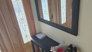 Un pasillo con una puerta de madera, un espejo, una mesita con un cuaderno y una cesta con zapatos.