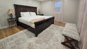 Un dormitorio con cama de madera, lámparas de noche, una ventana con cortinas traslúcidas y un banco junto a la ventana.