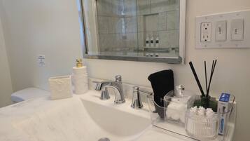 Un baño con lavamanos blanco, un espejo, inodoro y zona de ducha.