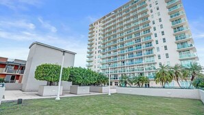 A modern high-rise building with multiple balconies, a well-maintained lawn, and a small building to the left. - Coconut Grove Suite | 20th Floor Bay Views (Miami)
