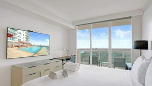 A modern hotel room with a large bed, a desk, a flat-screen TV, and a balcony with a pool view. - Coconut Grove Suite | 20th Floor Bay Views (Miami)