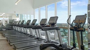 A row of treadmills in a gym with large windows offering a city view. - Coconut Grove Suite | 20th Floor Bay Views (Miami)