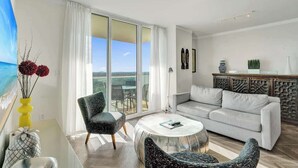A modern living room with a sofa, armchairs, a coffee table, and a view of the outdoors through large glass doors. - Bay View 1BR at The Arya in Coconut Grove (Miami)