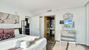 A hotel room with a large bed, a vanity with a mirror, and artwork on the walls. - Bay View 1BR at The Arya in Coconut Grove (Miami)