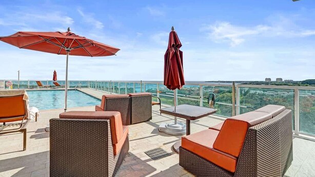 Eine Dachterrasse mit Korbmöbeln, einem Pool und einem Glasgeländer mit Blick auf eine Stadtlandschaft.