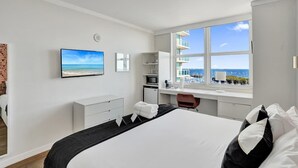 Ein modernes Hotelzimmer mit einem großen Bett, einem Schreibtisch, einem Fernseher und Meerblick.