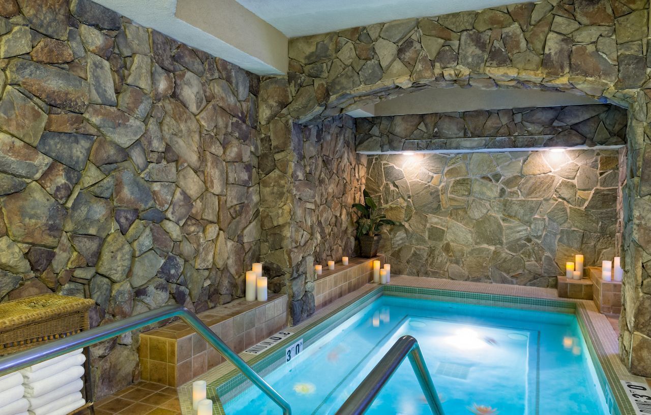 Une piscine intérieure aux murs de pierre, avec une eau d’un bleu limpide, un banc en pierre et des bougies.