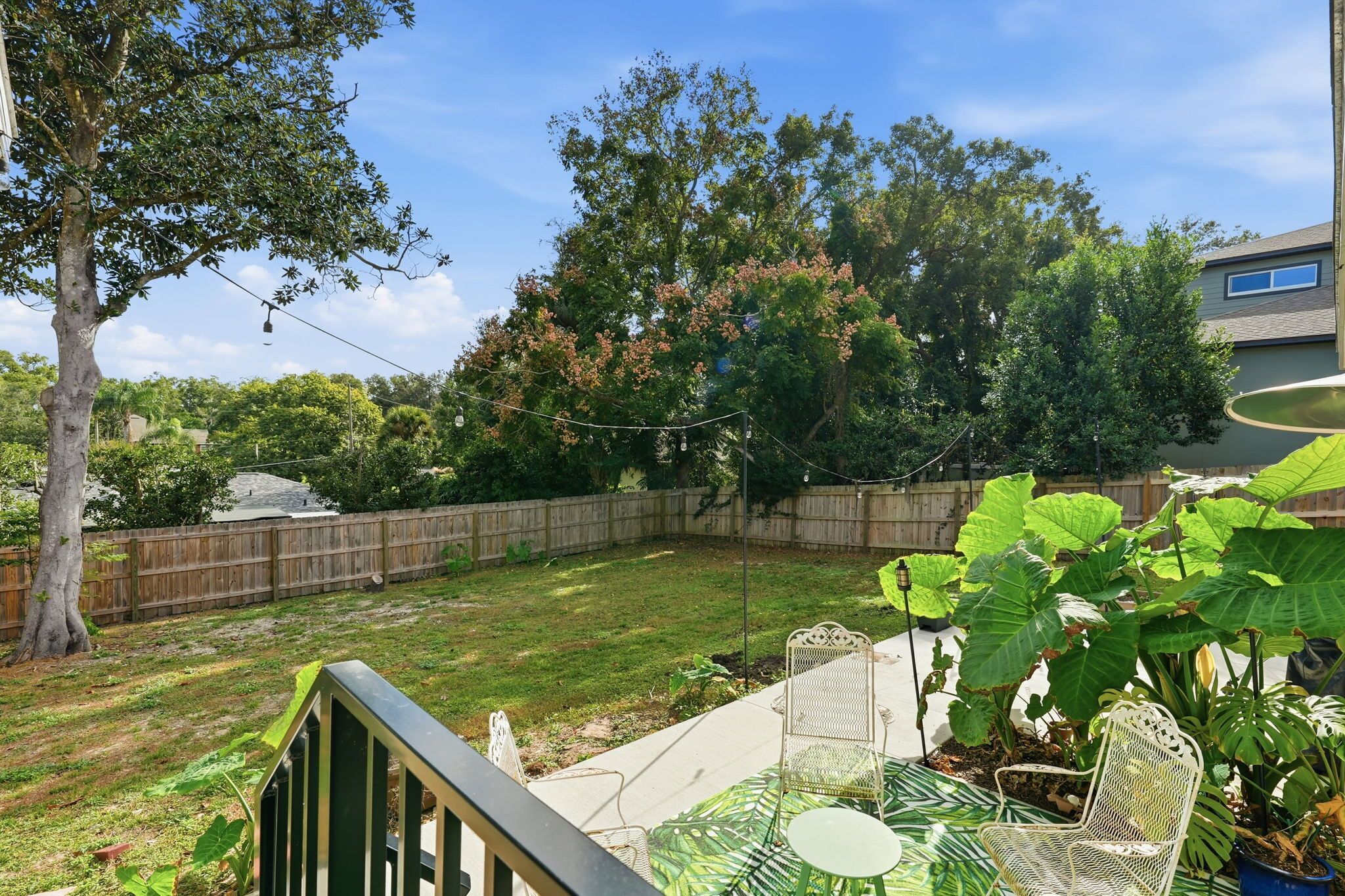 A backyard with a wooden fence, a grassy lawn, and a patio area with chairs and a table.