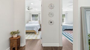 Een slaapkamer met een bed, een klein houten nachtkastje met een plant en een spiegel aan de muur.