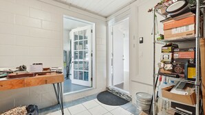 Een kamer met een houten bureau, een metalen plank met diverse spullen, en een deur naar een andere kamer.