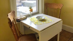 Pieni ruokailutila, jossa on valkoinen pöytä ja puinen tuoli, ikkuna, josta avautuu lumipeitteinen maisema, ja seinällä oleva kehystetty kuva.