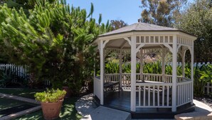 Een witte pergola met een bankje, omringd door potplanten en een wit hek.