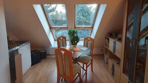 Pieni ja viihtyisä keittiö, jossa on ruokapöytä ja -tuolit, kaksi kattovalokuvioa ja ruukussa oleva kasvi.