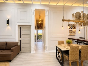 A room with a brown sofa, a dining table with wicker chairs, a hanging light fixture, and a view through an open door. - Modern 2BR King Suite • 5 Min to Baby Beach • Fast WiFi • Sleeps 4 (Ceru Colorado)
