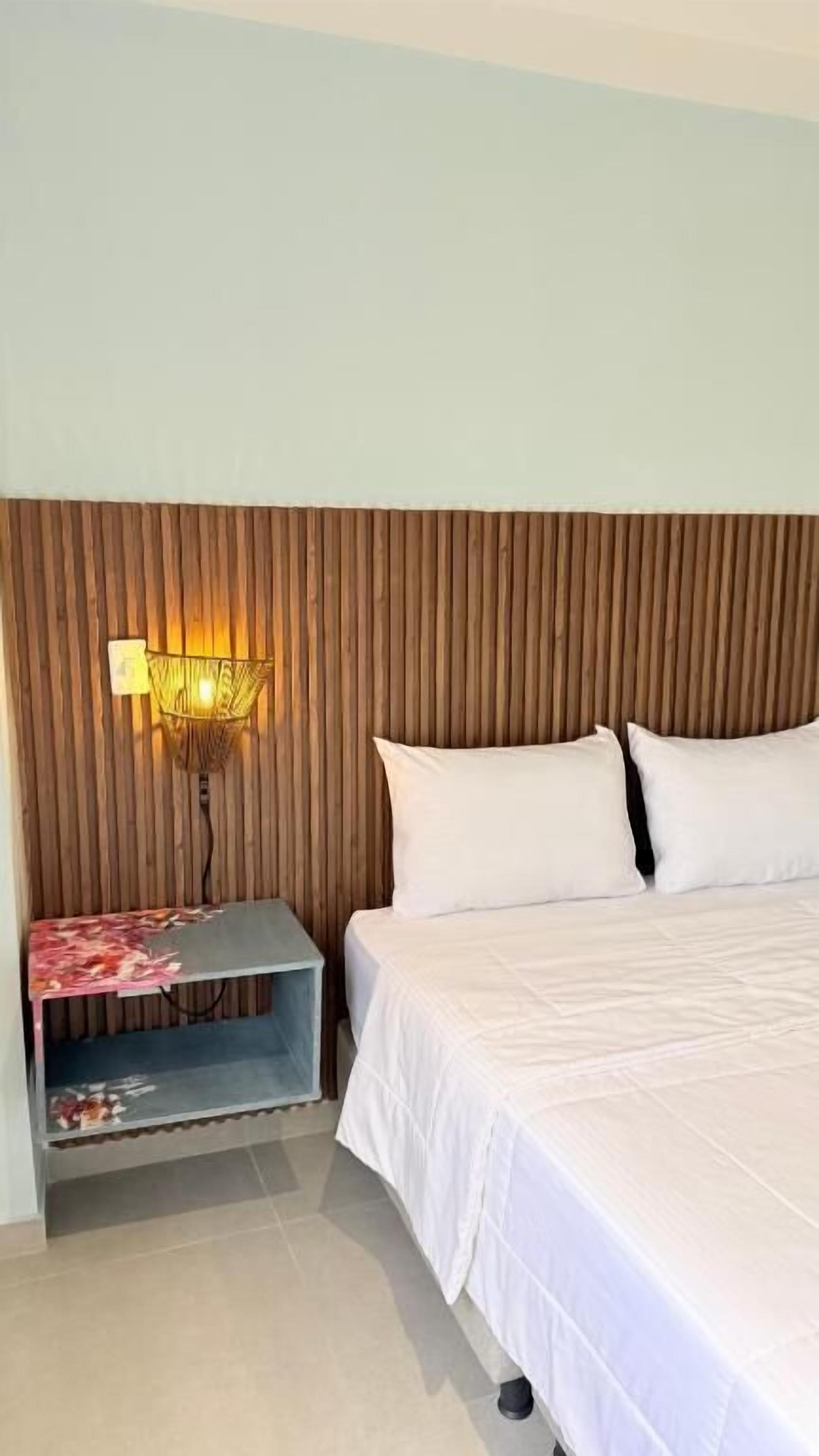 A hotel room with a bed, a nightstand with a lamp, and a small table with a floral tablecloth.