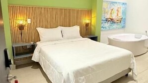 A modern bedroom with a large bed, a wooden headboard, bedside lamps, a round bathtub, and a painting on the wall. - Hotel Gallery Boutique (Pereira)