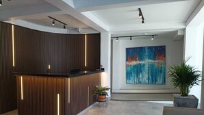 A modern reception area with a wooden reception desk, a large abstract painting on the wall, and a potted plant. - Hotel Gallery Boutique (Pereira)