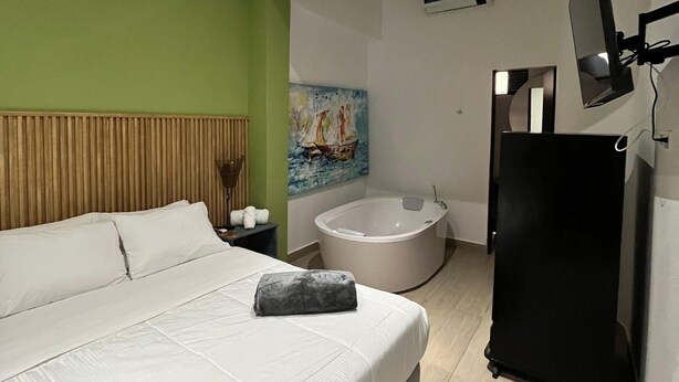 A modern hotel room with a large bed, a bathtub, a flat-screen TV, and a painting on the wall. - Hotel Gallery Boutique (Pereira)