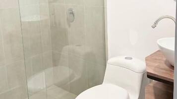 Een moderne badkamer met een douchecabine van glas, een wit toilet en een houten wastafelmeubel met een wastafel.