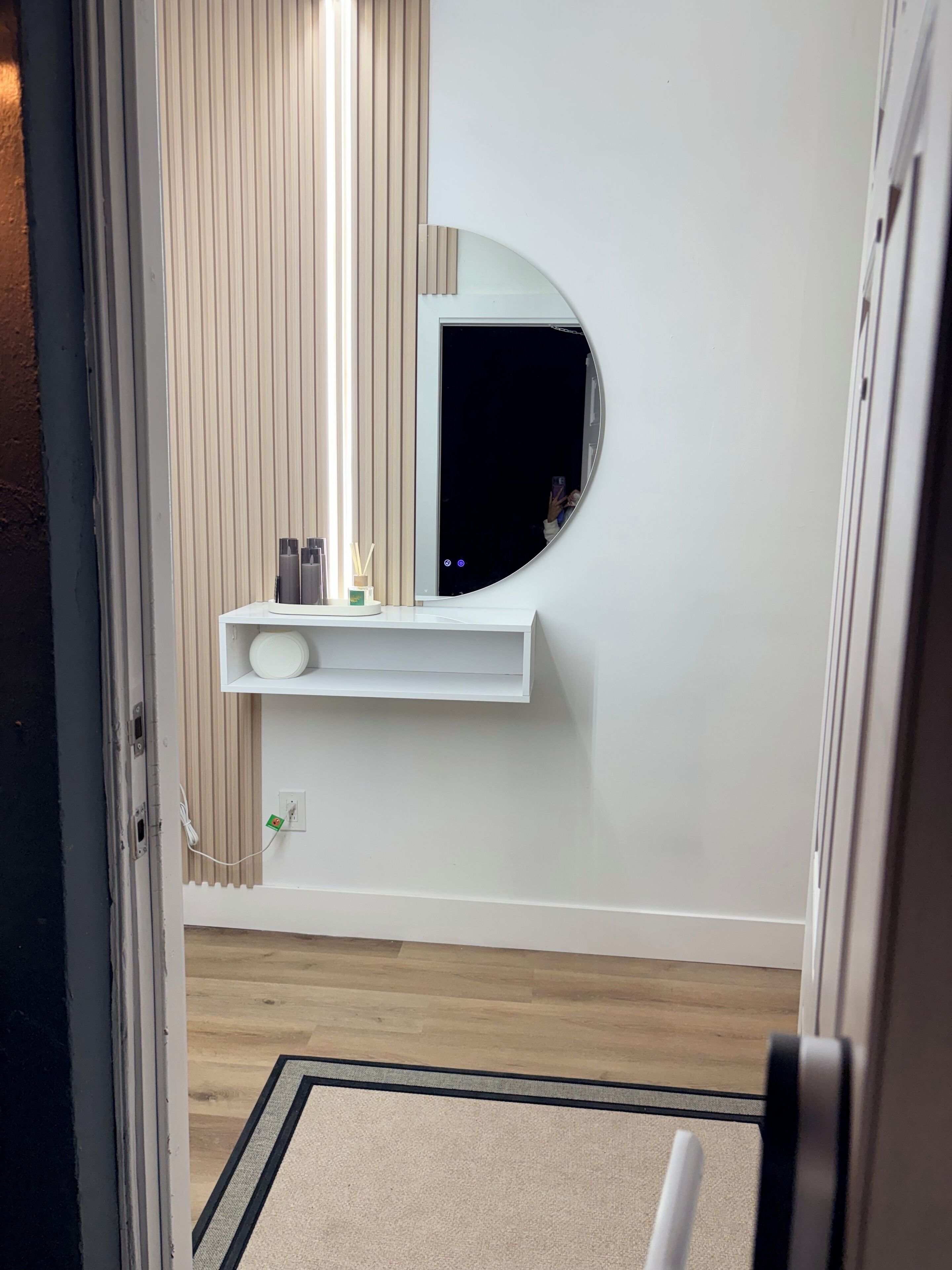 Un baño moderno con tocador blanco, un espejo redondo y suelo de madera.