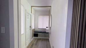 Ein schmales Entree mit einer Bank, einem Fenster mit Jalousien und einer Tür.