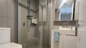 Ein modernes Badezimmer mit einer gläsernen Duschkabine, einer weißen Toilette und einem Waschbecken mit Spiegel.
