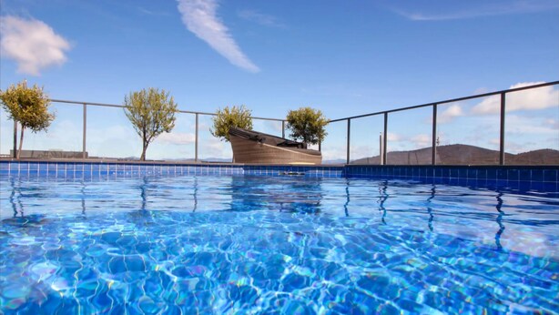 Ein Swimmingpool mit klarem, blauem Wasser, umgeben von einem Metallgeländer und zwei Bäumen.