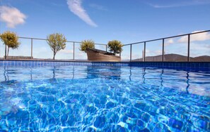 Una piscina con acqua cristallina e blu, circondata da un corrimano in metallo e due alberi.