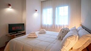 Une chambre d’hôtel avec un lit, un téléviseur affichant le logo de Netflix et une fenêtre avec des rideaux.