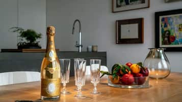 A bottle of Cristal champagne, four glasses, a fruit bowl, a key, and a vase on a wooden table.