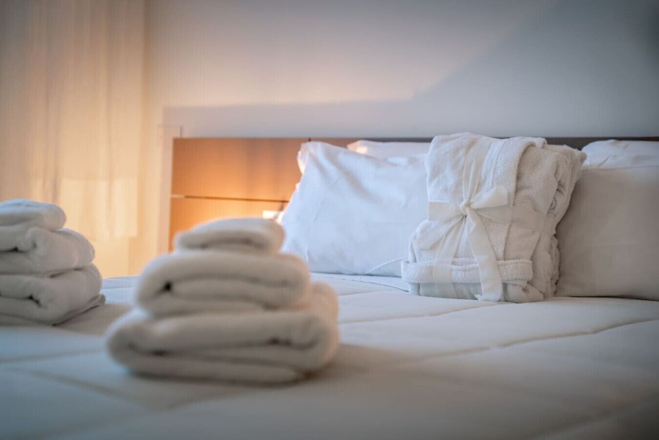 Un letto rifatto con lenzuola e asciugamani bianchi, una testiera e una lampada da comodino.