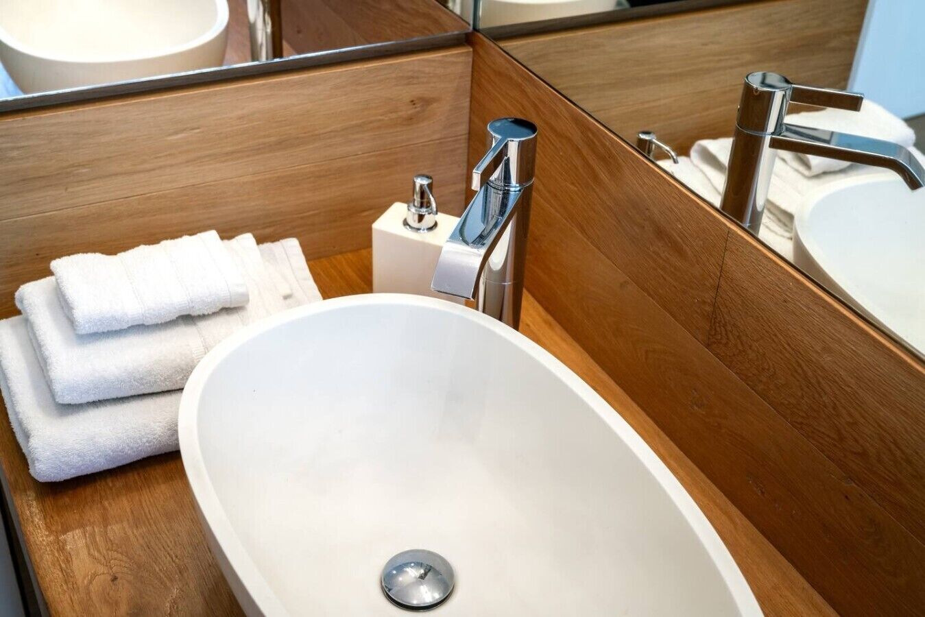 A bathroom with a white sink, a mirror, and a stack of white towels.