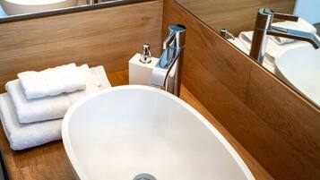 A bathroom with a white sink, a mirror, and a stack of white towels.