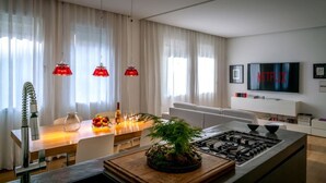 Une cuisine moderne équipée d’une cuisinière à gaz, d’une table à manger avec des chaises, de luminaires suspendus rouges et d’un téléviseur affichant le logo « NETFLIX ».