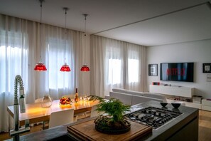 Una cocina moderna con estufa a gas, mesa de comedor con sillas, lámparas colgantes rojas y un televisor que muestra 'NETFLIX'.