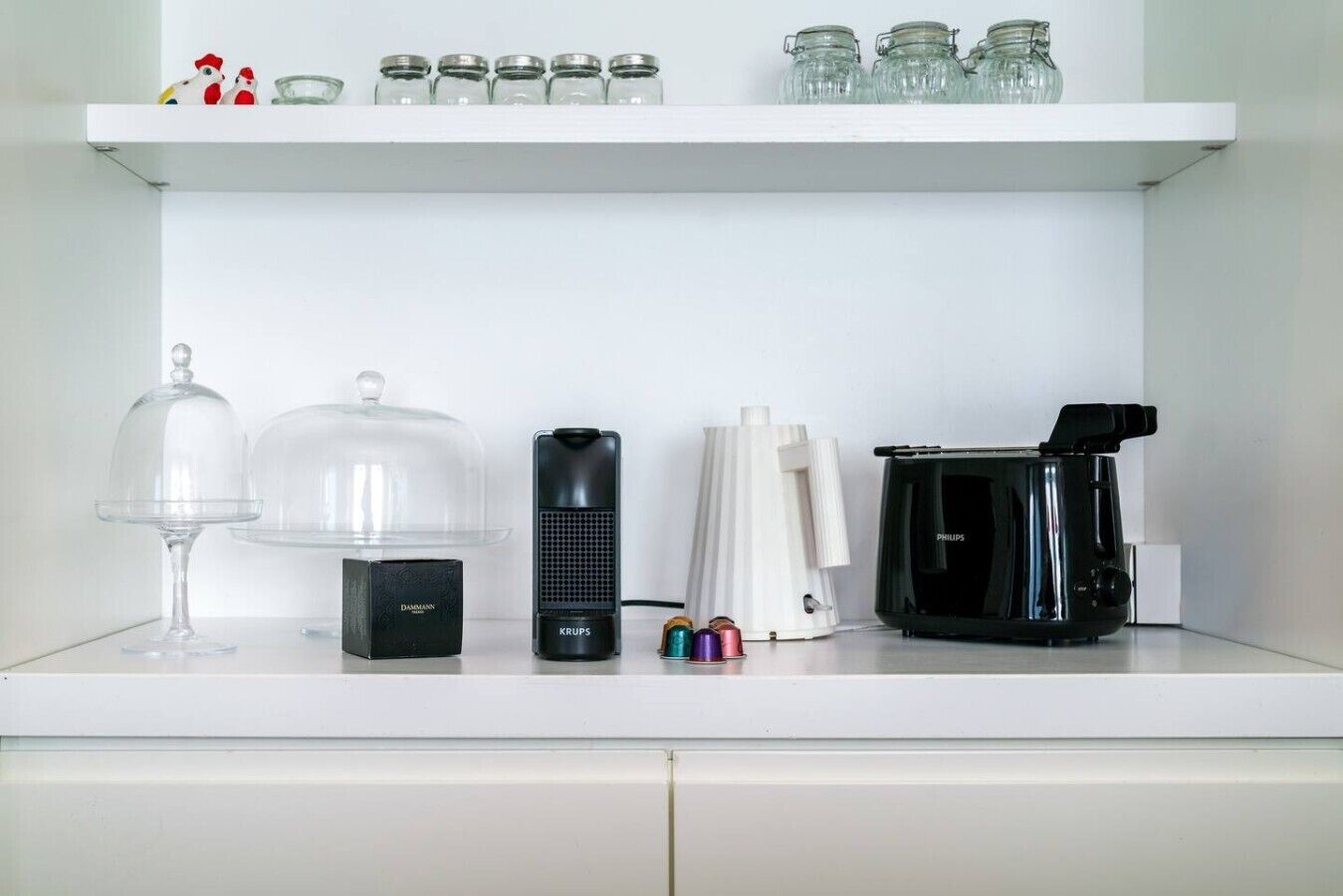 A kitchen counter with a coffee maker, a blender, a glass carafe, and a set of jars on a shelf.