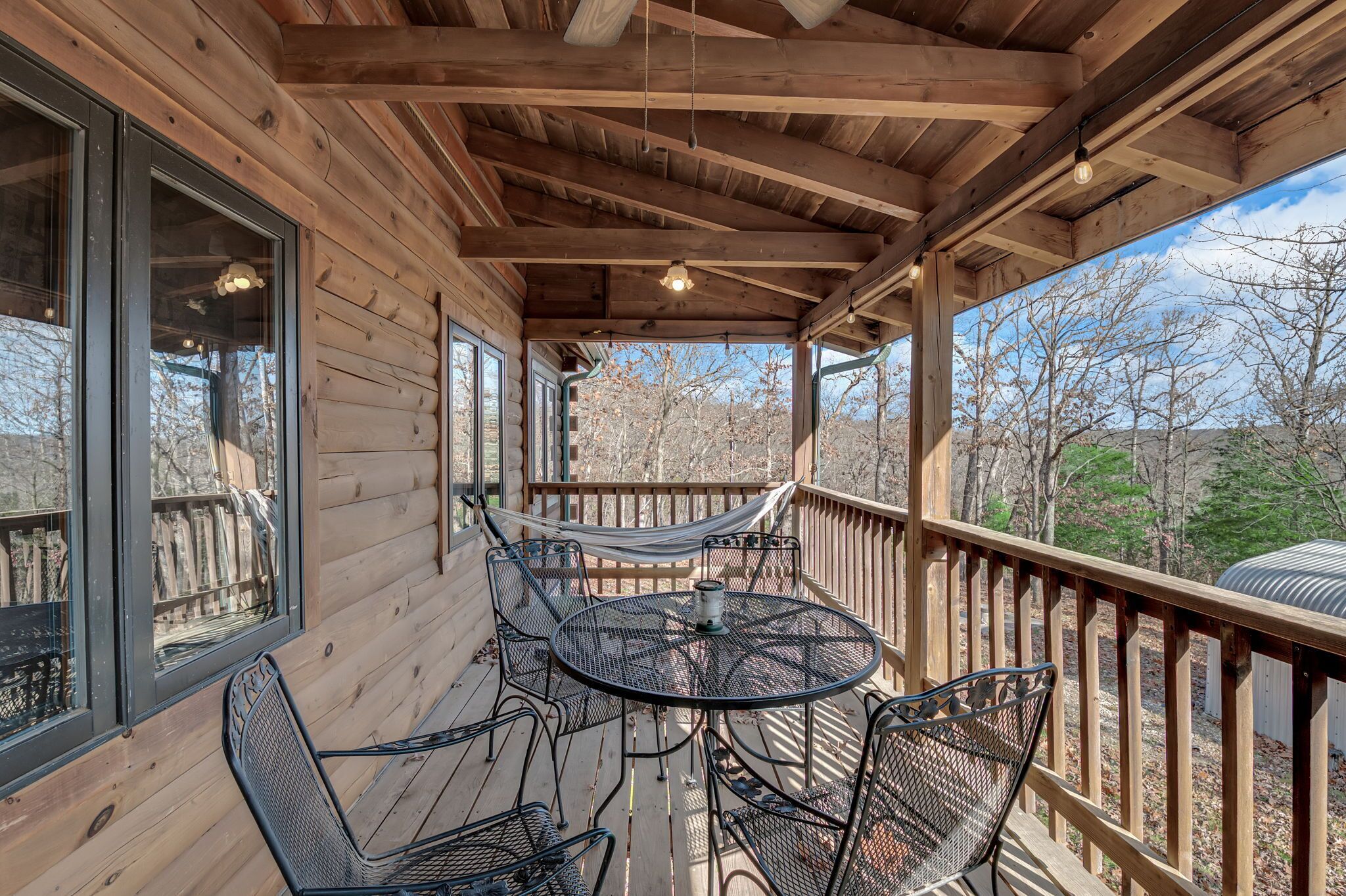 A wooden deck with a round table and chairs, a hammock, and a view of trees.